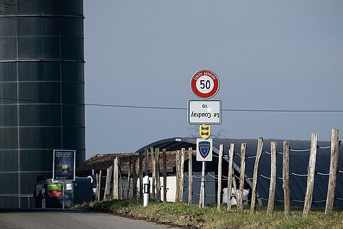 Ein verkehrt aufgehängtes Ortsschild vor einem Landwirtschaftsbetrieb.