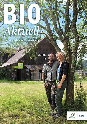 Ein Mann und eine Frau lehnen stehen bei einem Baum mit einem Hof im Hintergrund.