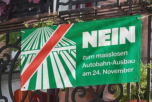 Eine grüne Fahne gegen Autobahnausbau an einem Balkon befestigt.