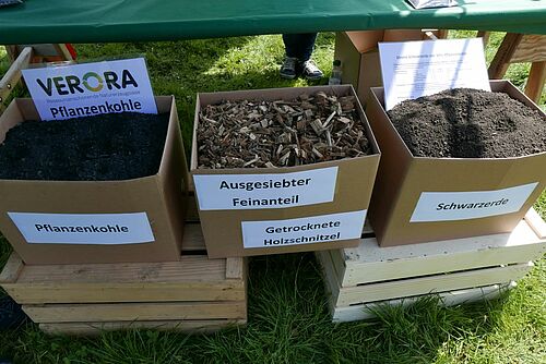 Drei Kartonschachteln, gefüllt mit Pflanzenkohle, Holzschnitzeln und Schwarzerde.