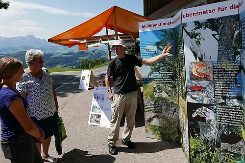 Zwei Zuhörerinnen und Hans Walter Krüsi stehen vor einer Infotafel.