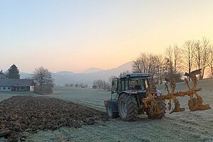 Traktor pflügt einen Acker in winterlicher Landschaft.